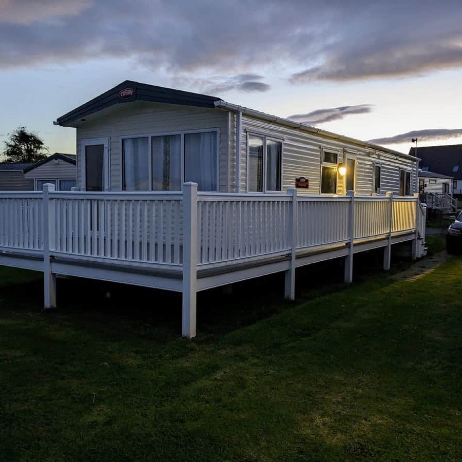 Modern white static caravan with decking at pet-friendly holiday park at dusk
