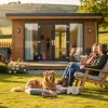 Couple sitting in lawn chairs outside a modern wooden cabin with a golden retriever resting on the grass nearby.